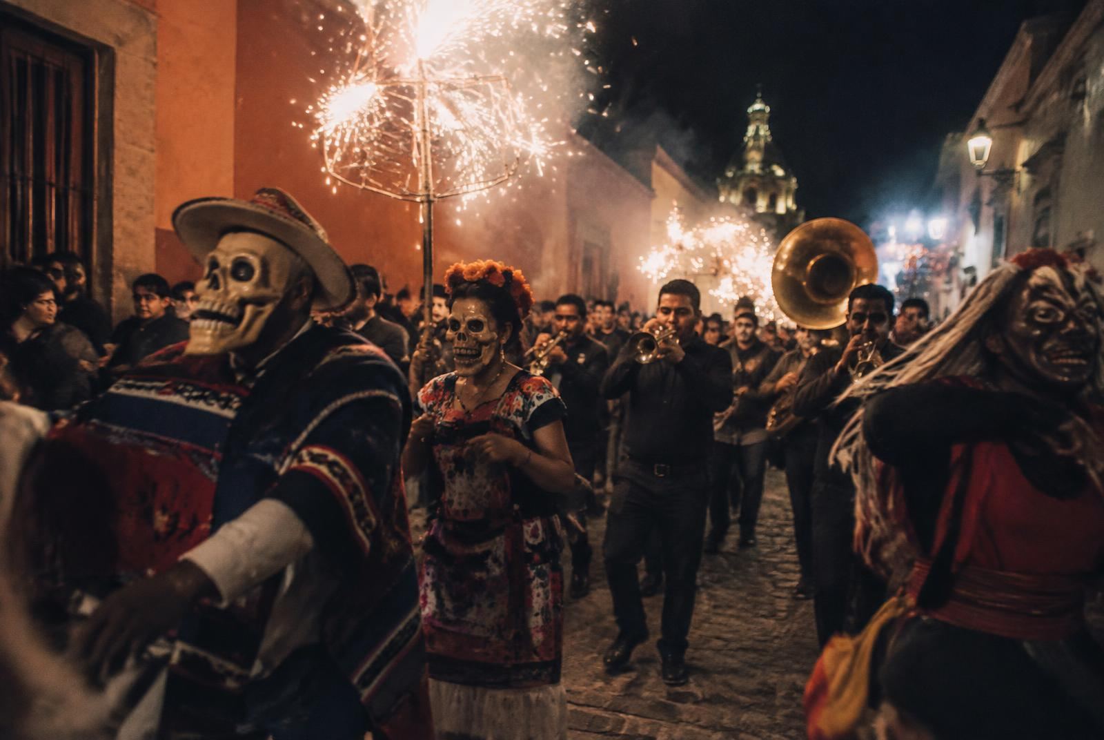 A comparsa winds through the streets with masks, brass and fireworks — part carnival, part prayer.