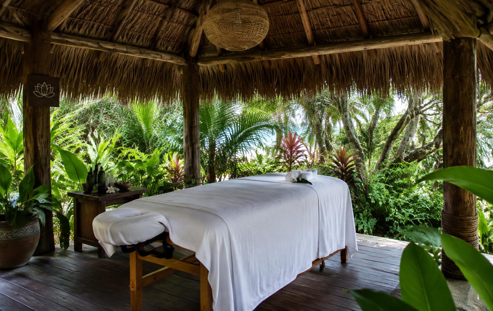 An open-air spa palapa surrounded by tropical plants